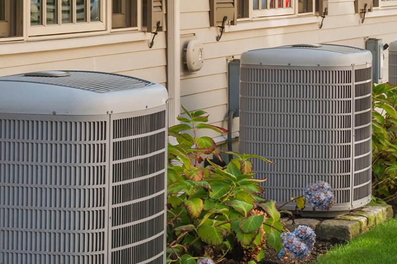 Spring AC Maintenance Tips. Two air conditioning units units next to blooming flowers.